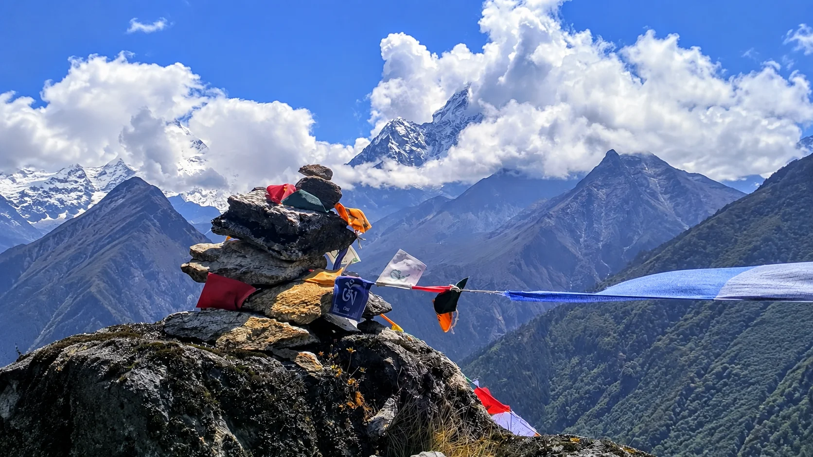 Prayer flags tied to a stone cairn beneath a Himalayan peak