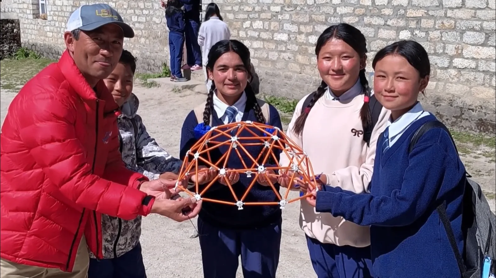 Students in Nepal holding a geodesic dome model with a community leader